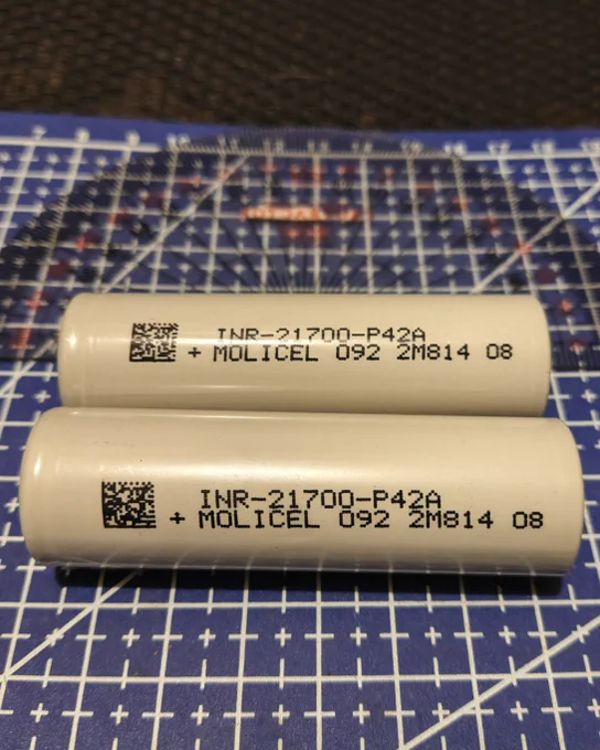2 grey 21700 battery cells on a cutting mat.