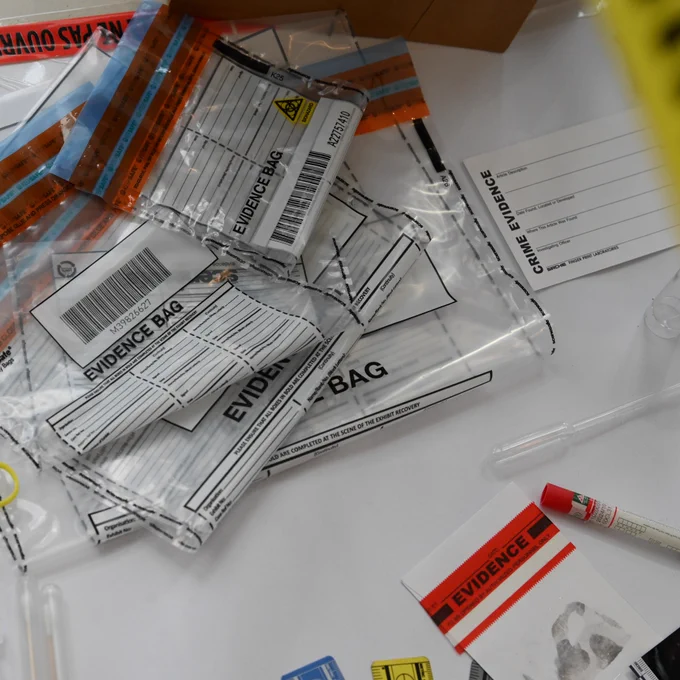 the image shows clear plastic evidence bags with barcodes and labels scattered on a white surface, alongside a fingerprint card and a red-capped marker.