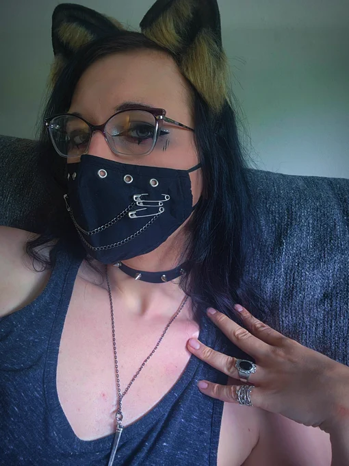 a picture of me sitting on the couch. im wearing raccoon ears and a face mask, a tank top, a spiked choker, and a necklace with a nail on it. my hand is resting on my shoulder