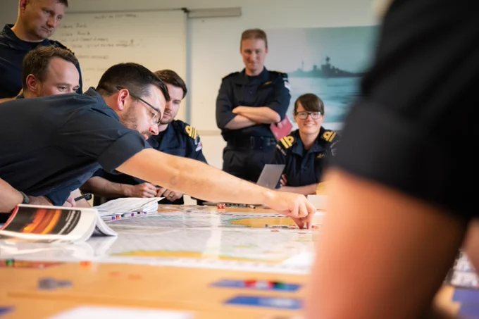 Group of uniformed officers gathered around a table studying maps and documents during a briefing session.