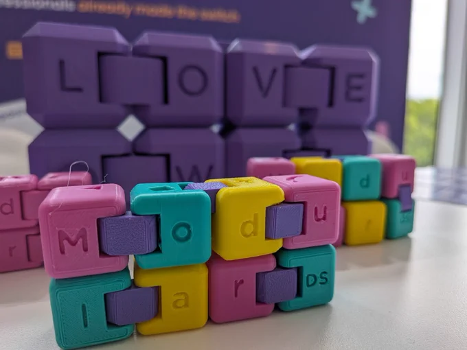 Colorful 3D-printed Modular DS fidget toys (infinity cubes) in pink, teal, yellow, and purple, displayed at the Modular DS booth at WordCamp Europe 2026.