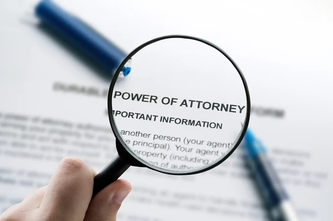 Magnifying glass highlighting the words 'Power of Attorney' on a legal document with a blue pen in the background.