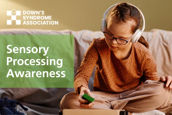 Image of a young girl who has Down's syndrome. She has headphone on and is sat on the floor in her bedroom. She is wearing glasses. 