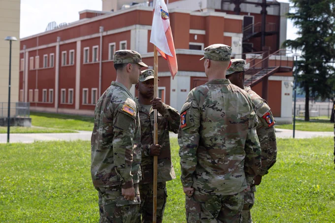 U.S. Army 1st Sgt. Joshua M. Pless Mosley, incoming first sergeant, Intelligence and Sustainment Company, Headquarters and Headquarters Battalion, U.S. Army Southern European Task Force, Africa (SETAF-AF), receives the guidon during the change of responsibility ceremony. Photo shows 4 Soldiers standing in field with guidon between them. 