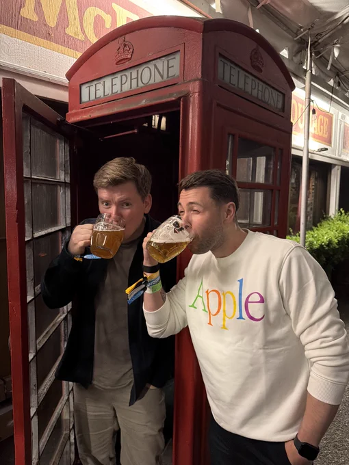 Photo of Aled and Tris drinking a pint in front of a red telephone box in a pub in California.