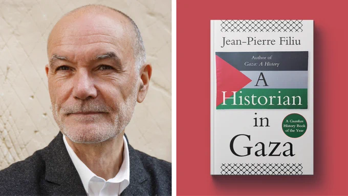 Jean-Pierre Filiu's author picture of him wearing a dark-coloured suit standing in front of a cream all, next to a mockup of his latest book, A Historian in Gaza. The cover features the Palestinian flag and black and white writing that reads 'A Historian in Gaza. Jean-Pierre Filiu. Author of Gaza: A History' and white writing in a green circle that reads 'A Guardian History Book of the Year'.