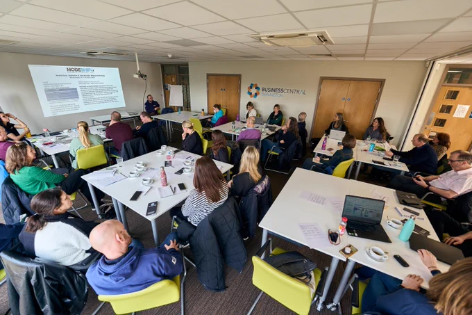 A group of professionals attending a business workshop in a conference room with a presentation projected on the wall.