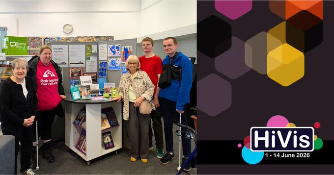 Group of five people standing around a display table with informational posters and books in a well-lit library. They are members of the Visually Impaired group at Newbattle Library, and are showing off a table with accessible reading formats on it. 