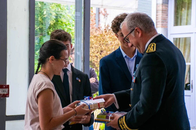 Le préfet des Hautes-Pyrénées remet un lot de livres attachés par un ruban tricolore à une jeune fille. À l'arrière-plan, deux jeunes hommes sourient lors de cette remise de prix officielle en intérieur.