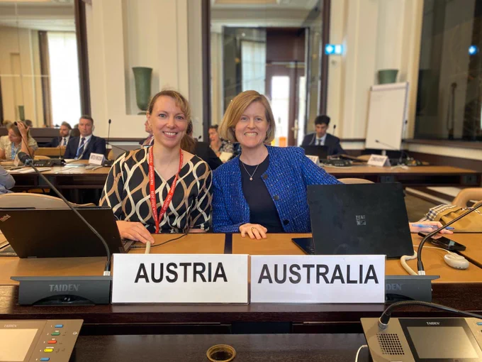 Photo of Australian and Austrian delegate posing behind their country nameplates.