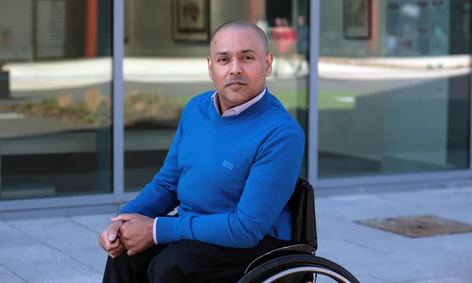 Photo of Kamran Mallick, a gentleman in a blue jumped sitting in a black manual wheelchair.