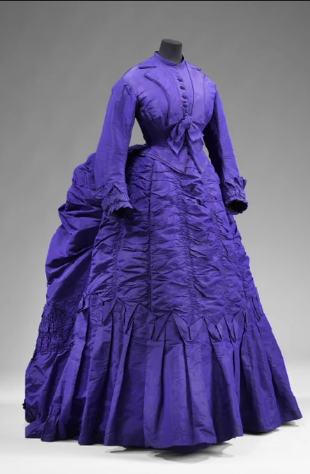 Front view of the early 1870s purple silk bustle dress which shows ruching down the front of the skirt, the draping of the bustle and the fitted buttoned bodice
