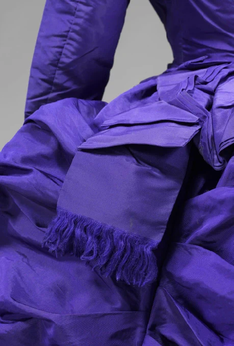 A detail of the bright purple 1870s bustle dress that focuses on the complex arrangement of the bustle centre back. It has a decorative bow with fringed edge