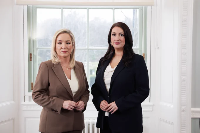 Image of two people - First Minister Michelle O’Neill and deputy First Minister Emma Little-Pengelly - standing in front of window.