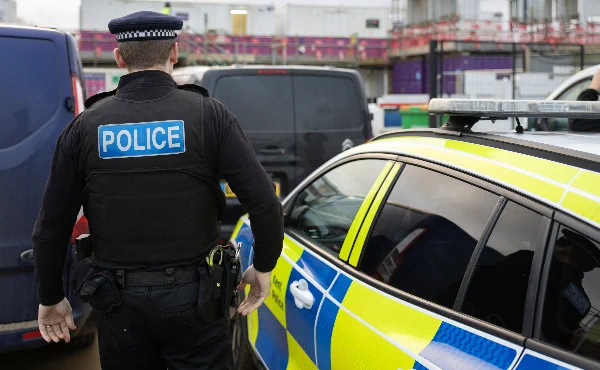 Photo of the back of a police officer standing beside a police car.