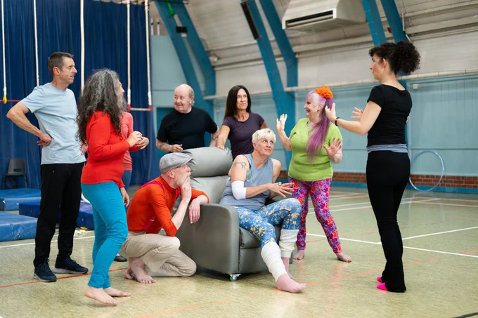A group of older people stand inside and chat together