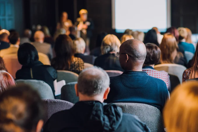 A room full of people viewed from behind seated in the audience at a TIS event. 