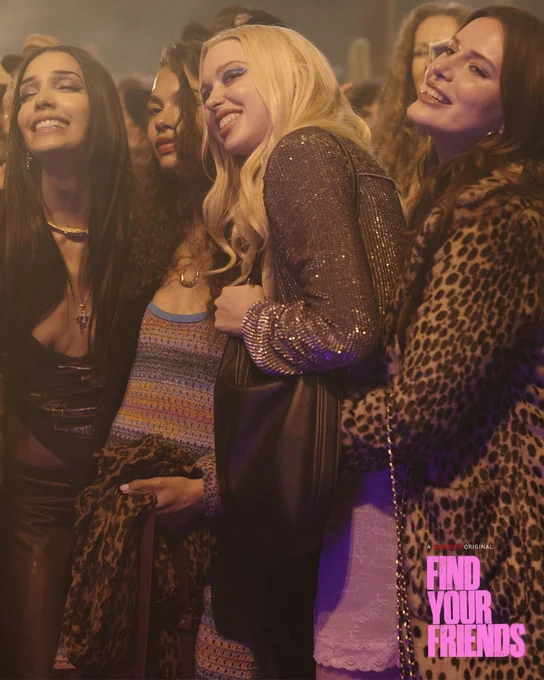 A group of four friends smiling and posing together in a lively nightclub setting. The ambient lighting and crowded background suggest a vibrant nightlife scene.