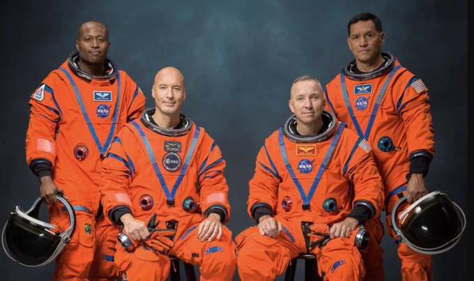 Artemis III crew in orange suits, left to right: Andre Douglas (standing left, holding helmet), Luca Parmitano (seated), Randy Bresnik (seated), and Frank Rubio (standing right, holding helmet). 
Official NASA portrait.