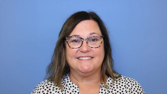 Smiling woman with glasses, against a blue background.