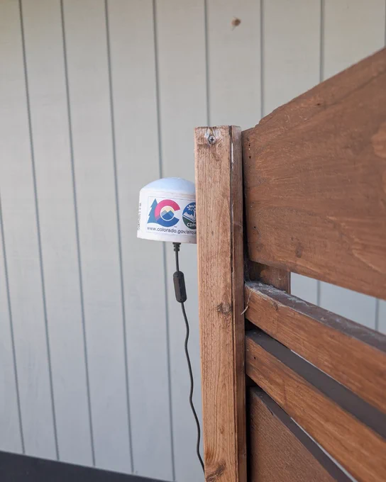 A white sensor outside with the CDPHE logo. 
