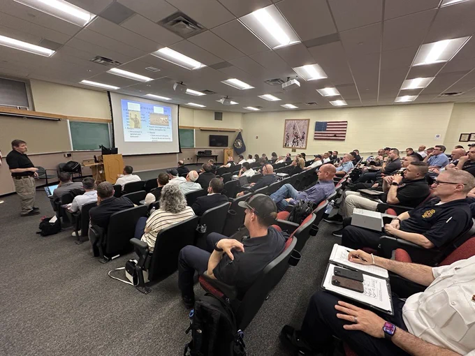 Wide angle shot of the Fire Academy auditorium with Curt Varone up front presenting to a crowd.