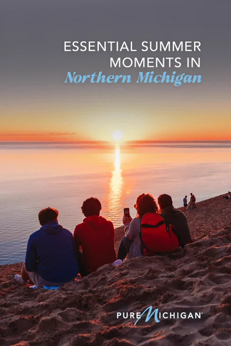 People sitting on a sandy dune overlooking a Lake Michigan sunset with overlay text reading Essential summer moments in Northern Michigan