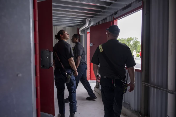 A group of emergency responders walks through a building, appearing to inspect the structure. The mood is serious and focused.