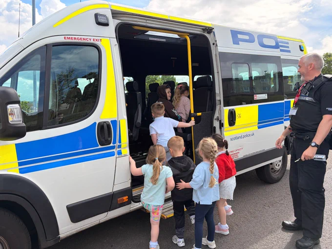 Police officer watches children boarding a Scotland Police van during a nursery visit.