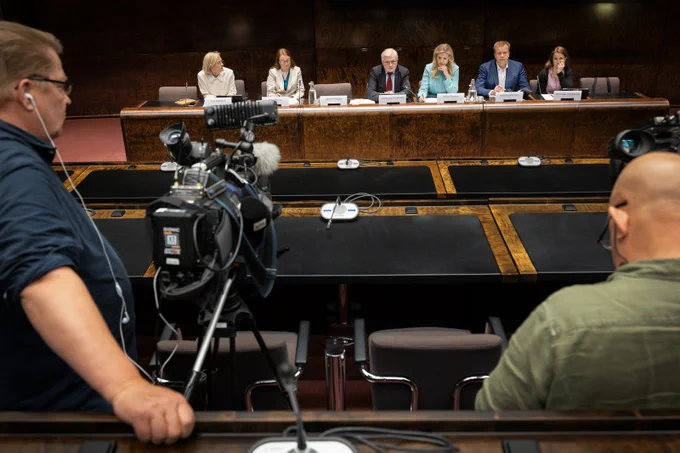 Ulkoasiainvaliokunnan kuusi kansanedustajaa istuu pitkän pöydän takana valiokunnan tiedotustilaisuudessa. Kuvan etualalla televisiokameroita ja -kuvaajia.