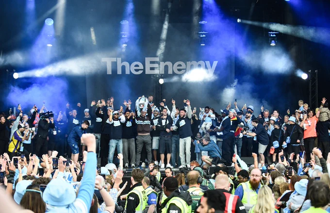 Coventry City Football Club celebrates on stage with a trophy, cheered by a large, phone-wielding crowd.