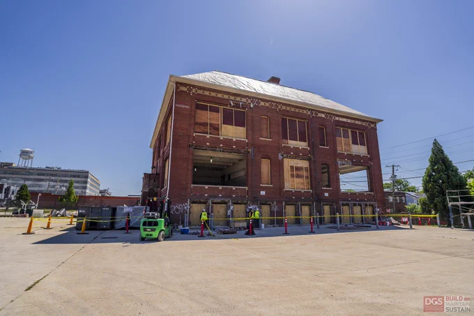 Old historic building, Crummell School under renovation with boarded windows and construction workers nearby on a sunny day.