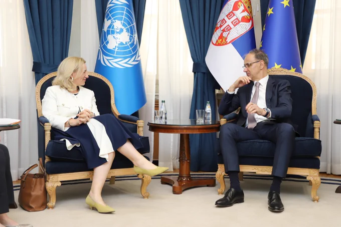 UNFPA Serbia Country Director Justine Coulson with Prime Minister of the Republic of Serbia, they are speaking and smiling. UN, Serbia and EU flags are behind them.