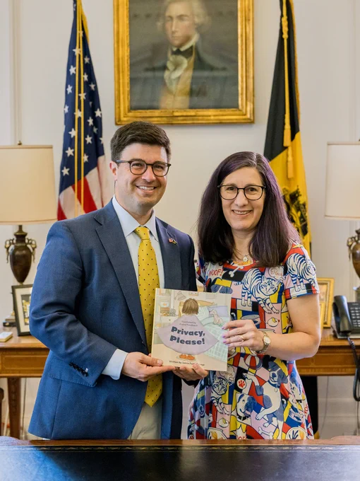 Photo of Mayor Corey O'Connor and Lorrie Cranor posing behind a desk in the mayor's office, holding a copy of the children's book "Privacy, Please!"