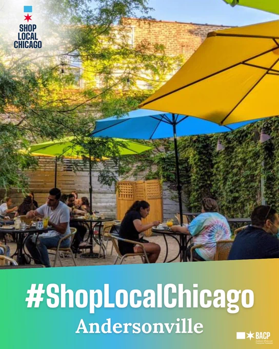 Outdoor patio dining with people seated at tables under large yellow and blue umbrellas. The setting has lush greenery on brick walls. Text overlay reads "#ShopLocalChicago Andersonville."