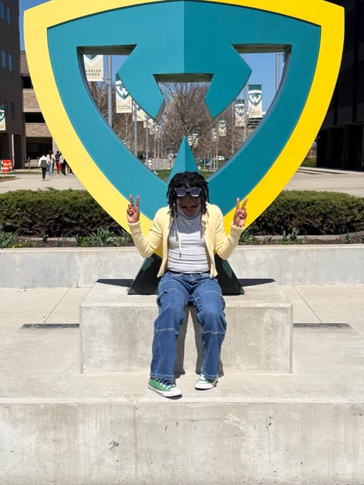 A person sits in front of the Wayne State University W statue with peace signs. 