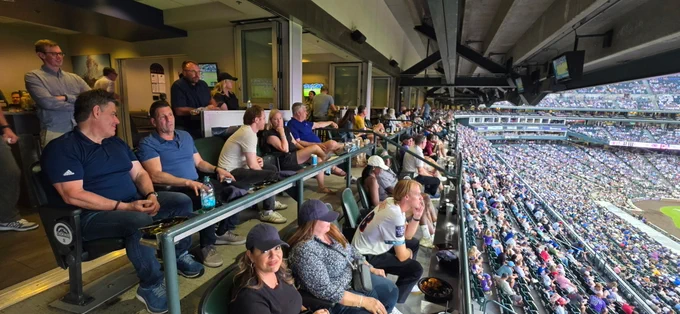 Crowd of spectators enjoying a baseball game from a covered stadium suite with a clear view of the field and stands.