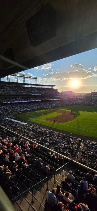 Sunset over a packed baseball stadium with fans watching the game on a clear day.