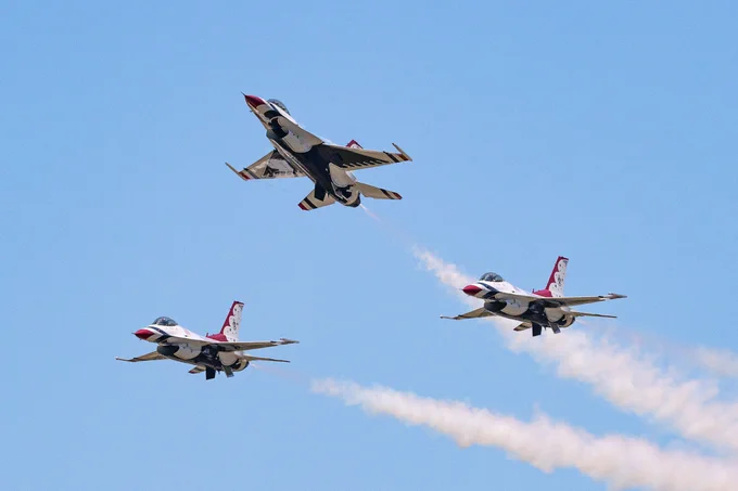 Three of the Thunderbird jets fly in a triangular formation against a light blue sky. The jets are red, white and blue, with white contrails trailing behind them. (Photo Credit: NASA/Terry Zaperach)