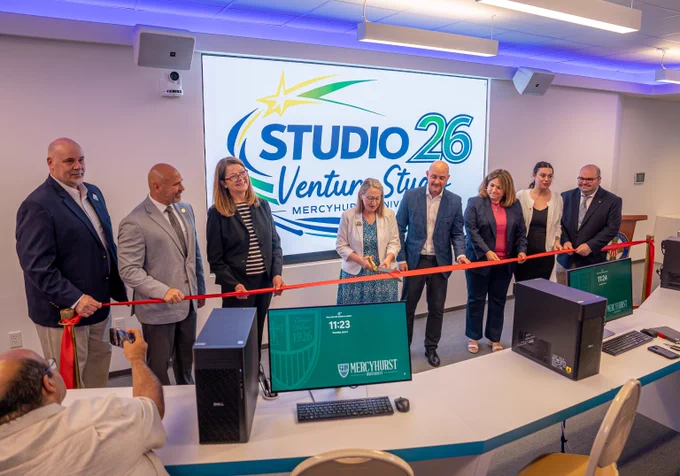 Group of seven people cutting a red ribbon during the opening ceremony of Studio 26 Venture Studio at Mercyhurst University.