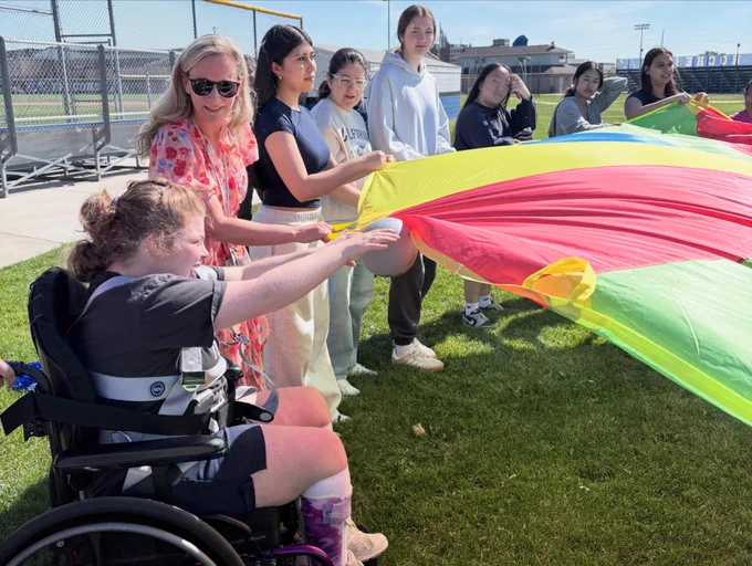 Group of diverse young people holding and lifting a colorful parachute outdoors on a sunny day at a sports field.