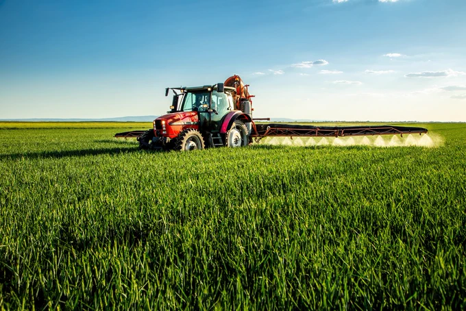 Tractor applying fertilizer to a field of growing crops.