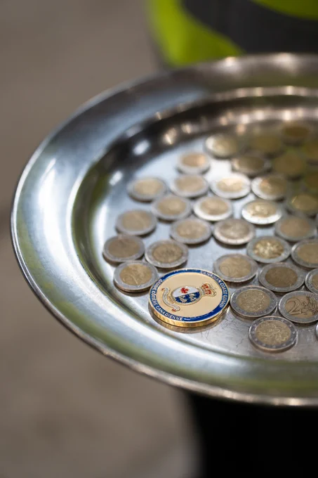 A metal tray holding several coins, including a distinctive coin in the center, in an indoor setting.