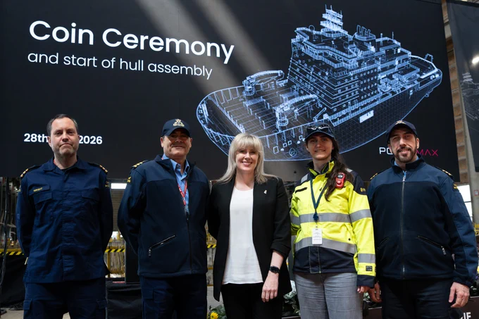 Five people pose in front of a screen reading “Coin Ceremony and start of hull assembly” with a ship diagram in the background.