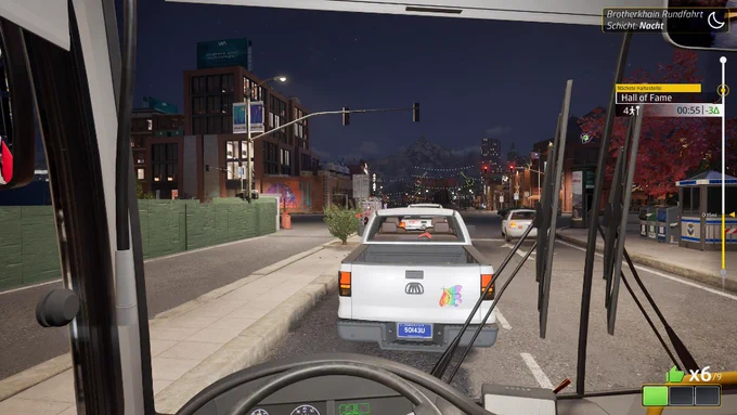 Nachtschicht im Bussimulator Bus Bound. Gameplay Screenshot aus dem Cockpit mit Blick auf die beleuchtete Stadt und einen voranfahrenden weißen Pickup Truck mit buntem Schmetterlingsaufkleber.
