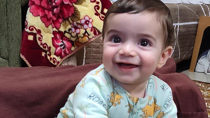 A photo of the Palestinian infant, 7 month old Sam Fahd Abu Haikal, smiling joyfully in his family home.