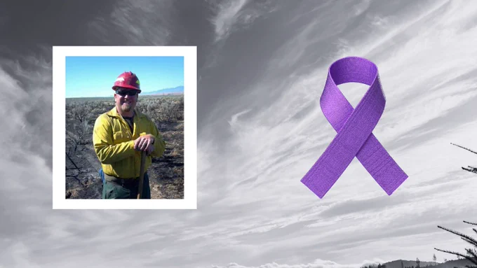 Person in yellow jacket and red cap standing in a dry, open landscape with sparse vegetation under a clear blue sky.