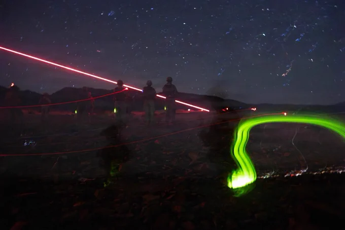 Tracer rounds cross the night sky as Marines conduct a live-fire exercise under limited visibility conditions in desert terrain.