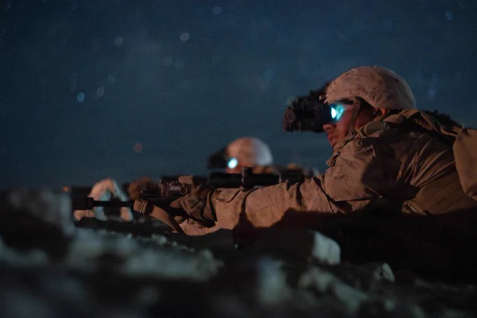 Marines fire from a prone position during a nighttime live-fire exercise, with a tracer round streaking across the desert sky.
