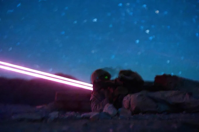 Marines fire from a prone position during a nighttime live-fire exercise, with a tracer round streaking across the desert sky.